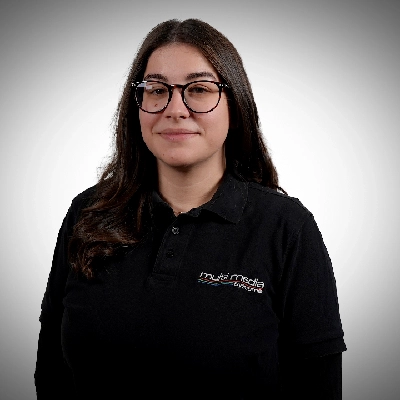 Celina-Lauterborn-400×400 Ein junge Dame, die ein schwarzes Poloshirt mit einem multi-media systeme Logo trägt, steht vor einem schlichten, hellgrauen Hintergrund.