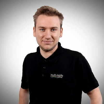 Evan-Maclnally-400×400 Ein junger Mann mit kurzen Haaren, der ein schwarzes Poloshirt mit einem multi-media systeme Logo trägt, steht vor einem schlichten, hellgrauen Hintergrund.