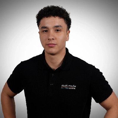 Marc-Deutscher-400×400 Ein junger Mann, der ein schwarzes Poloshirt mit einem multi-media systeme Logo trägt, steht vor einem schlichten, hellgrauen Hintergrund.
