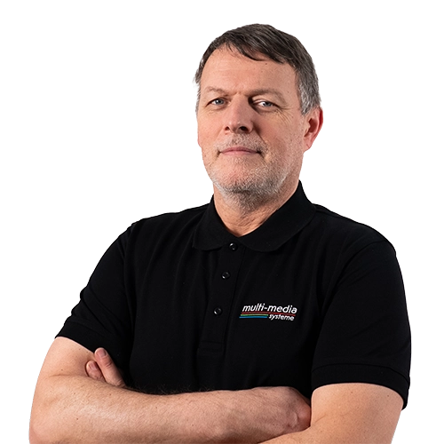 Ein Mann mit kurzen grauen Haaren, der ein schwarzes „Multimedia Systeme Service“-Polohemd trägt, steht mit verschränkten Armen vor einem schlichten weißen Hintergrund und blickt in die Kamera. Ein Mann mit kurzen grauen Haaren, der ein schwarzes „Multimedia Systeme Service“-Polohemd trägt, steht mit verschränkten Armen vor einem schlichten weißen Hintergrund und blickt in die Kamera.